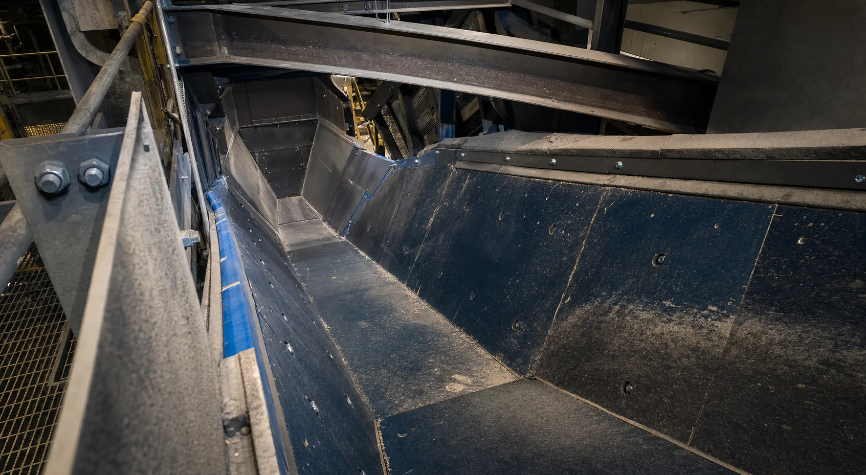 Concept view through an empty transfer chute with modular dark wear liners and a visible abrasion path.